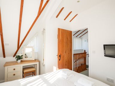 A bedroom with wooden beams a dressing table and a door leading to a staircase at Tyn Towyn - Ty Glas in Trearddur Bay