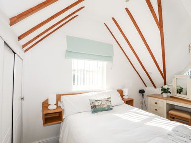 A bedroom with a bed beside a window and a desk with a mirror and flower on it at Tyn Towyn - Ty Glas in Trearddur Bay
