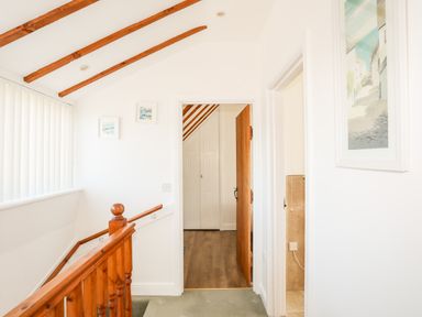 A hallway with wooden handrail and beams leading to a room with wooden floor and white closet doors at Tyn Towyn - Ty Glas in Trearddur Bay