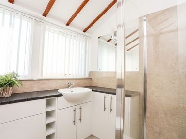 A bathroom with a countertop sink white cabinets a mirror and a shower at Tyn Towyn - Ty Glas in Trearddur Bay