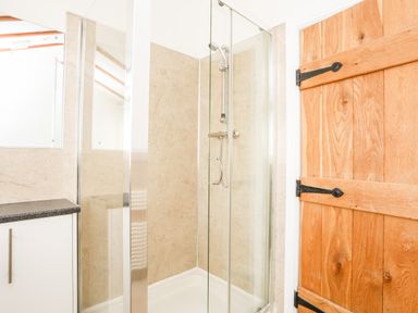 A bathroom with a glass shower enclosure a wooden door and a countertop with cabinets at Tyn Towyn - Ty Glas in Trearddur Bay