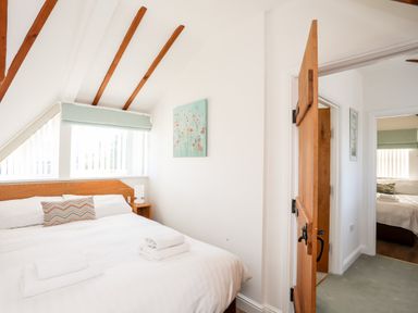 A bedroom with a double bed two folded towels a bedside table lamp and an open wooden door at Tyn Towyn - Ty Glas in Trearddur Bay