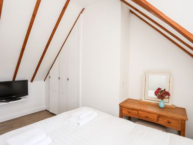 A bedroom with a bed towels a wooden dressing table with a mirror and flowers a wall-mounted television and built-in closets at Tyn Towyn - Ty Glas in Trearddur Bay