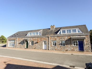 A stone building with three doors and multiple windows along a street at Tyn Towyn - Ty Glas in Trearddur Bay