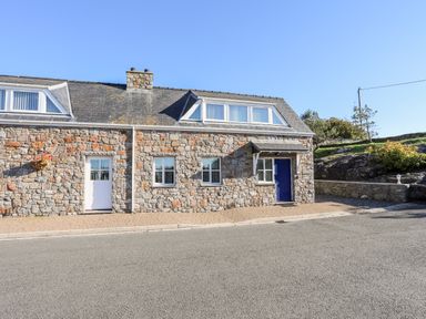 A stone house with two doors and three windows on a paved area at Tyn Towyn - Ty Glas in Trearddur Bay