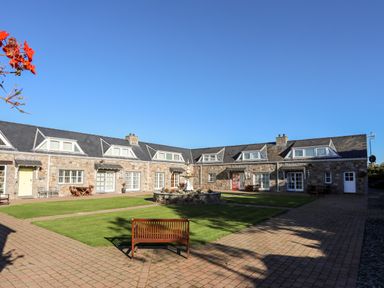 A courtyard with benches and a stone fountain surrounded by stone buildings at Tyn Towyn - Ty Glas in Trearddur Bay
