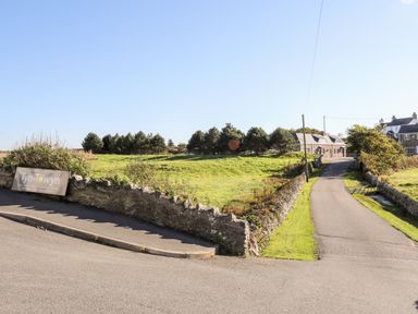 A road leading to buildings with a stone wall and open grassy area at Tyn Towyn - Ty Glas in Trearddur Bay