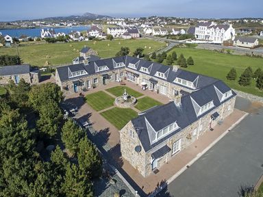 An aerial view of a U shaped stone building with a central courtyard and green lawn at Tyn Towyn - Ty Oren in Trearddur Bay