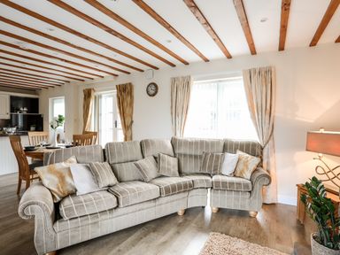 A living room with a striped sectional sofa and cushions near windows with curtains and wooden beams on the ceiling at Tyn Towyn - Ty Oren in Trearddur Bay