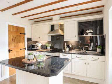 A kitchen with white cabinets an island with plants a wooden door and appliances at Tyn Towyn - Ty Oren in Trearddur Bay