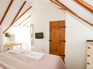 A bedroom with a bed folded towels a wooden door a wall-mounted tv a mirror a wooden desk with a vase of flowers at Tyn Towyn - Ty Oren in Trearddur Bay