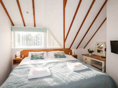 A bedroom with a double bed two pillows two folded towels bedside tables dressing table and television at Tyn Towyn - Ty Oren in Trearddur Bay