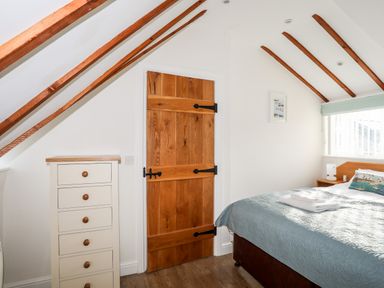 A bedroom with a wooden door a chest of drawers and a bed with a blue bedspread at Tyn Towyn - Ty Oren in Trearddur Bay