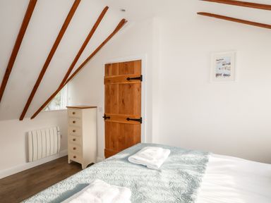 A bedroom with a bed covered in a light blue quilt and white towels next to a wooden door and a small drawer chest at Tyn Towyn - Ty Oren in Trearddur Bay