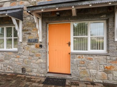 A stone exterior wall with an orange door and windows at Tyn Towyn - Ty Oren in Trearddur Bay