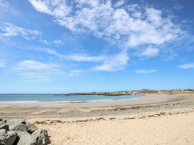 A sandy beach with rocks and calm sea under a partly cloudy sky at Tyn Towyn - Ty Oren in Trearddur Bay