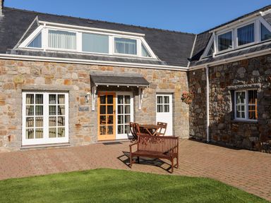A stone building exterior with a patio area containing wooden bench and table set at Tyn Towyn - Ty Oren in Trearddur Bay