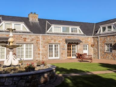 A stone building with multiple windows and a door with outdoor furniture and a white decorative fountain in front at Tyn Towyn - Ty Oren in Trearddur Bay