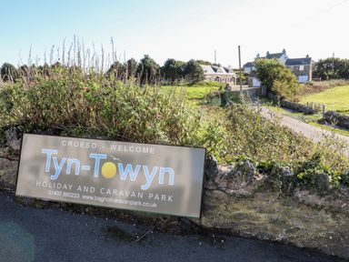 A sign for Tyn Towyn holiday and caravan park by a stone wall with bushes and houses in the background at Trearddur Bay
