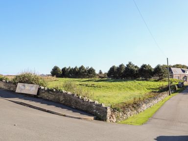 A roadside view of a grassy field with stone walls and a sign for Tyn Towyn holiday and caravan park near Trearddur Bay