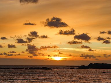 A sunset over the ocean with scattered clouds and rocky formations at Tyn Towyn - Ty Oren in Trearddur Bay