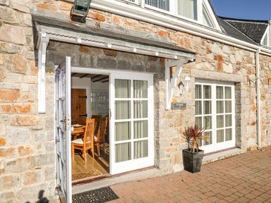 Stone building exterior with white framed glass doors and wooden chairs visible inside at Tyn Towyn - Ty Piws in Trearddur Bay