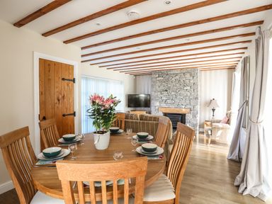 A dining area with a wooden table and chairs and a stone fireplace in a living room at Tyn Towyn - Ty Piws in Trearddur Bay