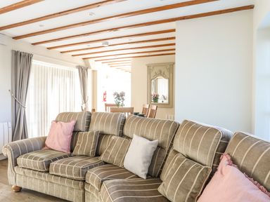 A living room with a striped sofa and cushions near a dining area with wooden chairs and a wall mirror at Tyn Towyn - Ty Piws in Trearddur Bay