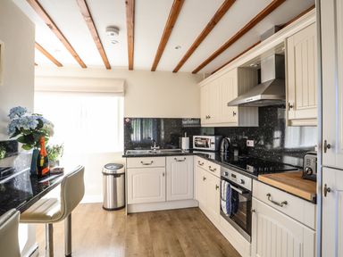 A kitchen with white cabinets black countertops stainless steel appliances and wooden ceiling beams at Tyn Towyn - Ty Piws in Trearddur Bay