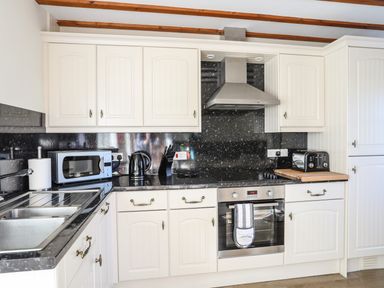 A kitchen with white cabinets black countertop microwave kettle toaster and oven at Tyn Towyn - Ty Piws in Trearddur Bay