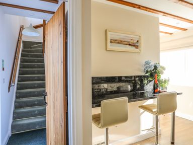 A hallway with stairs and a small dining area with two chairs at Tyn Towyn - Ty Piws in Trearddur Bay
