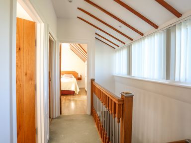 A hallway with wooden railing and beams leading to a bedroom at Tyn Towyn - Ty Piws in Trearddur Bay