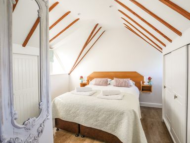 A bedroom with a double bed pillows and towels under a ceiling with exposed wooden beams at Tyn Towyn - Ty Piws in Trearddur Bay