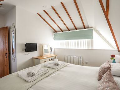 A bedroom with a bed, folded towels on the bed, a small TV mounted on the wall and a dresser with a mirror at Tyn Towyn - Ty Piws in Trearddur Bay