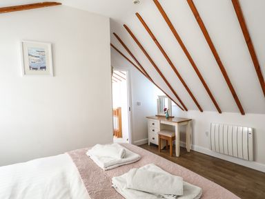 A bedroom with a bed with folded towels a dressing table with a mirror and stool and exposed wooden beams on the ceiling at Tyn Towyn - Ty Piws in Trearddur Bay