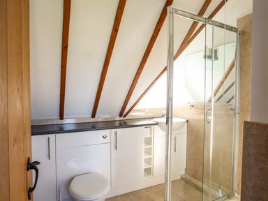 A bathroom with white cabinets a toilet a sink a mirror and a glass shower enclosure at Tyn Towyn - Ty Piws in Trearddur Bay