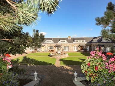 A stone building surrounding a courtyard with a fountain and green lawn at Tyn Towyn - Ty Piws in Trearddur Bay