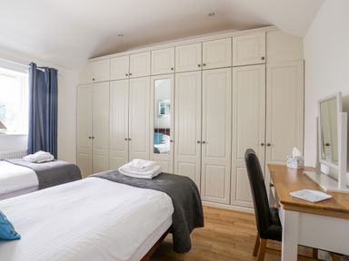 A bedroom with two beds and a large wardrobe with a mirror and a desk with a chair at Tyn Towyn - The Stables in Trearddur Bay