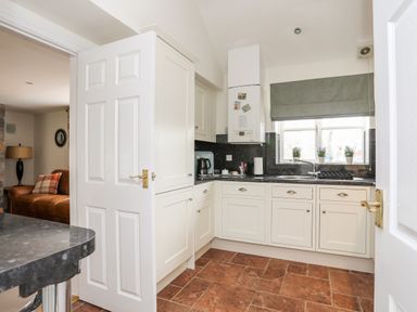 A kitchen with white cabinets black countertop and a window with plants at Tyn Towyn - The Stables in Trearddur Bay
