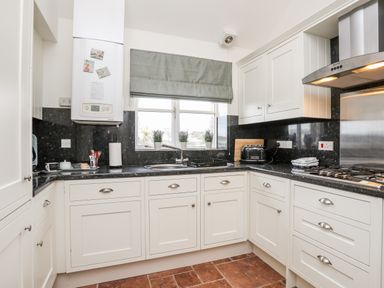 A kitchen with white cabinets black countertops a window with three potted plants and a stove at Tyn Towyn - The Stables in Trearddur Bay