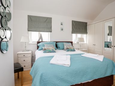 A bedroom with a bed covered in blue bedding and white towels on top with bedside tables and lamps at Tyn Towyn - The Stables in Trearddur Bay