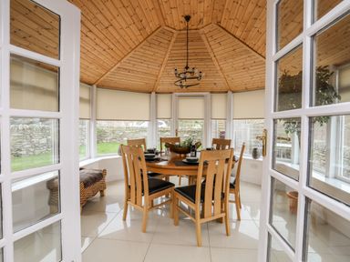 A dining area with a round wooden table and six chairs under a wooden ceiling at Tyn Towyn - The Stables in Trearddur Bay