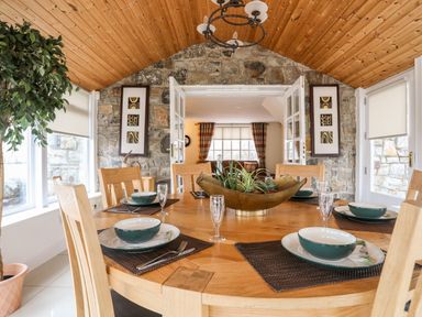 A dining table set for six with bowls and glasses in a room with stone walls and wooden ceiling at Tyn Towyn - The Stables in Trearddur Bay