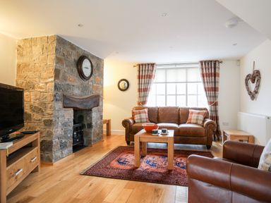 A living room with a stone fireplace a leather sofa and armchair a wooden coffee table and a television at Tyn Towyn - The Stables in Trearddur Bay