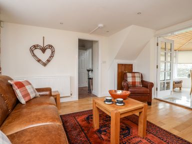A living room with leather sofa and armchair a wooden coffee table and a heart-shaped wall decoration at Tyn Towyn - The Stables in Trearddur Bay