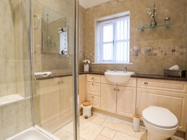 A bathroom with a shower, sink, toilet, cabinets, and a window at Tyn Towyn - The Stables in Trearddur Bay