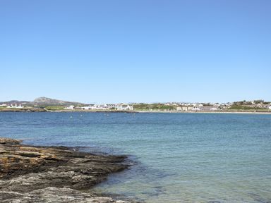 A coastal view with rocky shore in the foreground and a small town with houses across the water at Tyn Towyn - The Stables in Trearddur Bay