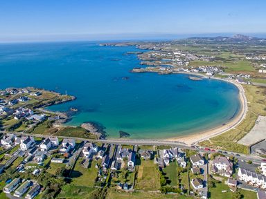 A coastal village with houses along a curved sandy beach and blue sea at Tyn Towyn - The Stables in Trearddur Bay