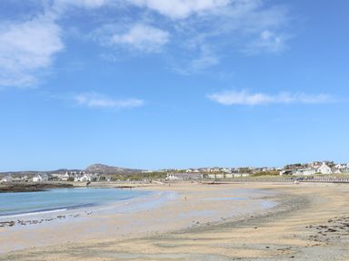 A sandy beach with calm water and buildings along the shoreline at Tyn Towyn - The Stables in Trearddur Bay