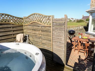 An outdoor patio with a hot tub wooden fence wooden table with chairs and a barbecue grill at Tyn Towyn - The Stables in Trearddur Bay